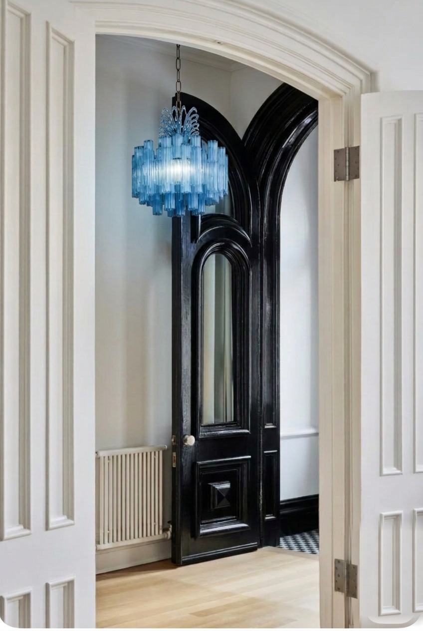 A hallway entrance with a large blue glass chandelier hanging above an arched white doorway and a glossy black door.