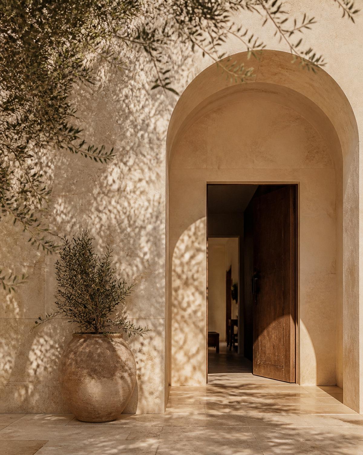 Sunlit stone archway and olive shadow at the threshold of a private residence.